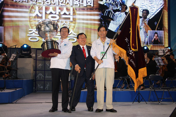 지난 10일 막을 내린 제30회 전국장애인체육대회에서 종합우승 5연패를 달성한 경기도선수단 한성섭 총감독(오른쪽)과 도 체육진흥과 오재영 팀장(왼쪽)이 윤석용 대한장애인체육회장으로부터 우승기와 우승배를 전달받은 뒤 기념촬영을 하고 있다. /사진제공=경기도장애인체육회