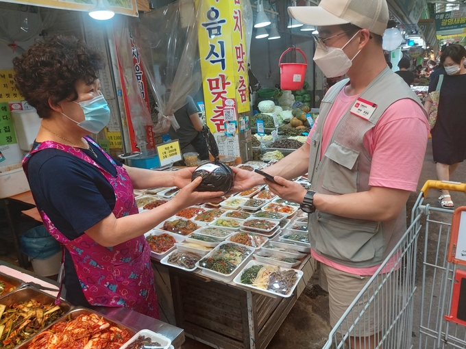 6일 놀장 유성요 광명센터장이 경기 광명시 광명전통시장의 한 반찬가게에서 주문 물품을 전달받고 있다. (사진=편지수기자)