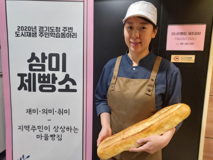 장예원 ㈜일공일오컴퍼니 대표가 미나리식빵 빵공장 앞에서 바게트를 들고 웃고 있다. (사진=편지수 기자)
