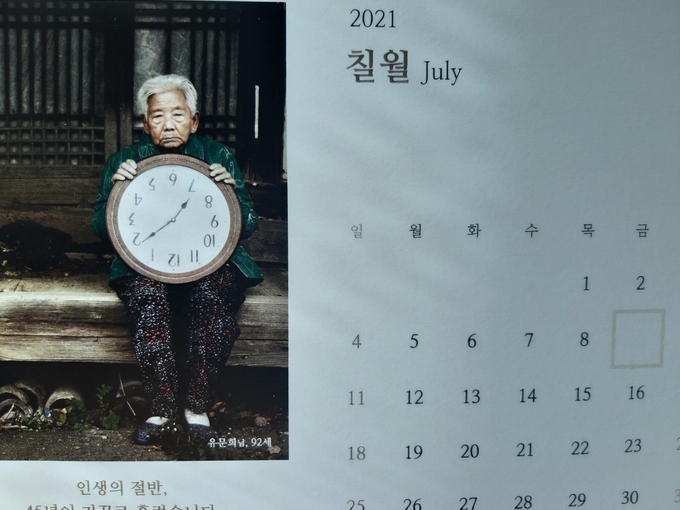  “인생의 절반, 45년이 거꾸로 흘렀습니다”라는 문구와 함께 유문희 할머니(92)가 시계를 거꾸로 들고 있는 모습이 담긴 7월달 달력. 상수원보호구역으로 묶인 9일자 칸이 비워있다.(사진=이화우 기자)