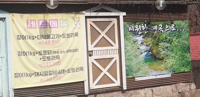 깨끗한 계곡 사진과 '시원한 계곡으로...'라는 문구의 현수막 옆 14만원 상당의 메뉴가 담긴 현수막도 함께 걸려있다. (사진 = 박환식 수습기자)