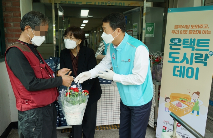 서명철 국민건강보험공단 인천경기지역본부장(오른쪽)이 6일 경기 수원시 우만종합사회복지관에서 독거 어르신께 어버이날 기념 카네이션과 도시락을 전달하는 모습. (사진=국민건강보험공단 인천경기지역본부 제공)