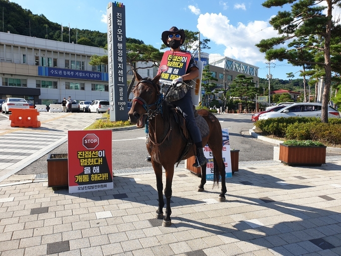 오남진접발전위원회 관계자가 진접·오남 행정복지센터 앞에서 말을 타고 '진접선 개통' 등 촉구하는 내용을 알리고 있다. (사진=오남진접발전위원회 제공)