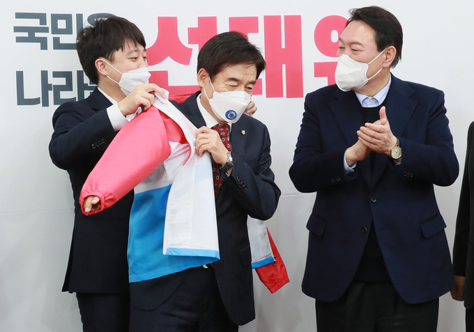 국민의힘 이준석 대표가 7일 오후 국회에서 국민의힘에 입당한 무소속 이용호 의원에게 당복을 입혀주고 있다. 오른쪽은 윤석열 대선 후보. (사진=국회사진기자단/연합뉴스)