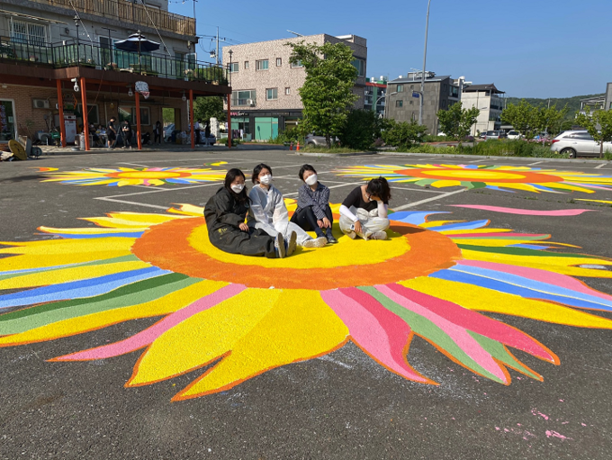 파주희망일자리사업에 참여한 여성들이 법원읍 거리에서 자신들이 그린 그림 위에 앉아있다.(사진=파주시 제공) 