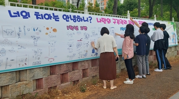 '너의 치아는 안녕하니?' 나만의 구강관리 파우치에 그린 그림을 신양중학교 외벽에 부착, 학생들과 학부모가 그림을 살펴보고 있다.(사진=김포시보건소 제공)