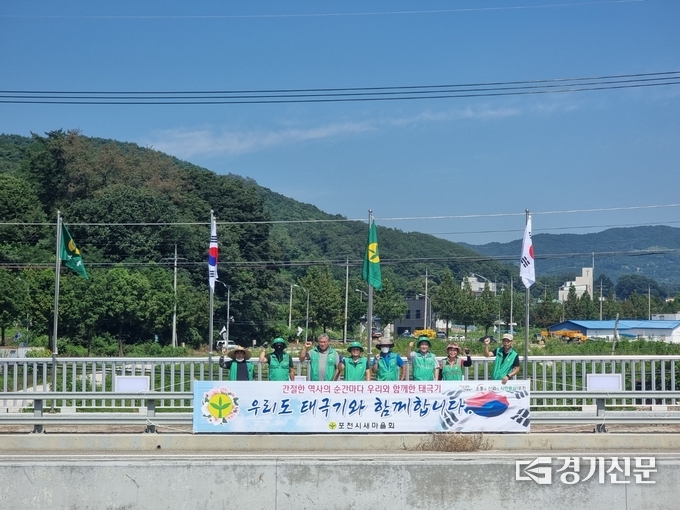 용정교 위에 태극기를 게양한 새마을회 회원들이 기념촬영하고 있다. (사진=포천시 제공)
