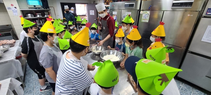 BBQ 치킨대학의 치킨캠프에 참여한 아이들이 황금올리브 치킨 조리하는 방법을 설명 듣고 있다. (사진=제너시스BBQ 제공)