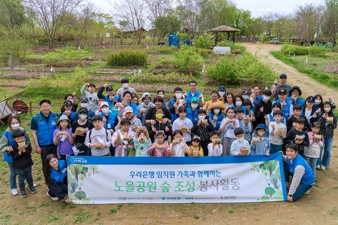 봉사활동에 참여한 임직원 및 가족들이 묘목을 들고 기념촬영을 하고 있다. (사진=우리은행 제공)