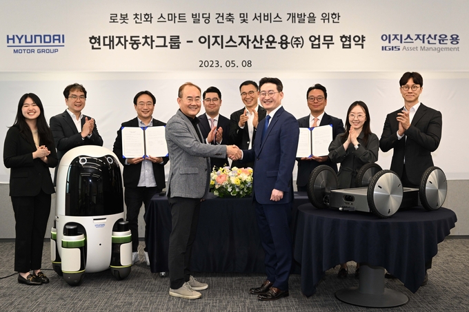 현대차∙기아의 실내외 배송 로봇(왼쪽)과 모베드(MobED, 오른쪽)가 놓인 가운데 현대차∙기아 연구개발본부장 김용화 부사장(앞줄 왼쪽)과 이지스자산운용 리얼에셋부문 정석우 대표(앞줄 오른쪽)가 기념 사진을 촬영하고 있다. (사진=현대차그룹 제공)