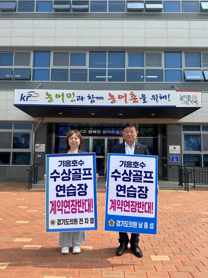 경기도의회 더불어민주당 소속 남종섭(용인3, 오른쪽) · 전자영(민주·용인4) 의원이 15일 한국농어촌공사 평택지사 앞에서 ‘기흥호수 수상골프 연습장 계약연장반대!’가 적힌 피켓을 들고 1인 시위에 나섰다. (사진=경기도의회 남종섭 의원실 제공)