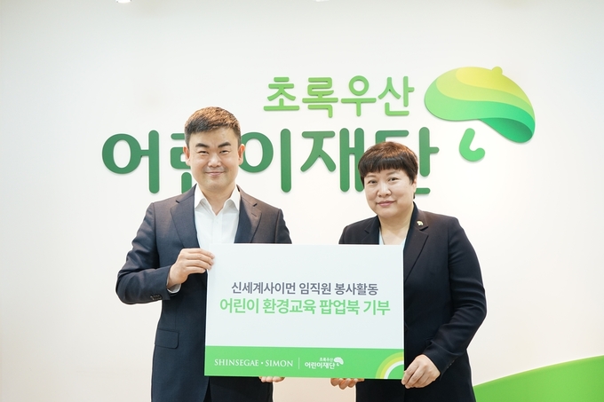 신세계사이먼이 초록우산어린이재단에 어린이 환경교육 팝업북을 기부했다. (사진 왼쪽 신세계사이먼 이현수 CSR팀장, 오른쪽 초록우산어린이재단 최운정 서울2지역본부장).(사진=신세계사이먼 제공).