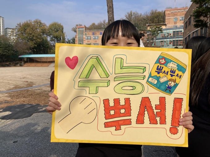 15일 조원고 1학년 학생이 3학년 수험생 선배들을 위해 자체제작한 푯말을 들고 웃고 있다. (사진=이보현 기자)