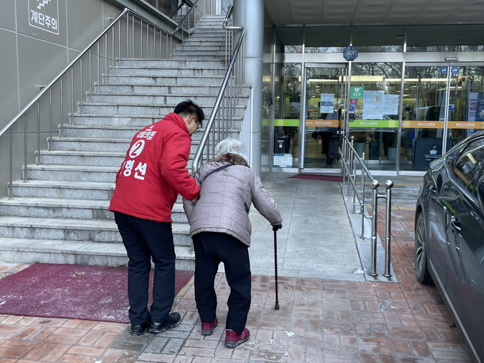 홍형선 예비후보가 노인복지회관에 오시는 어르신을 부축해 회관으로 모시고 들어가고 있다( 홍 예비후보 선서사무소 제공)