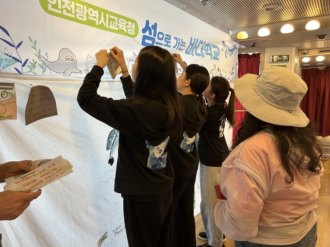  돌아오는 배편에서 폐현수막을 재활용한 메모지에 소감을 적어 붙이고 있는 학생들. ( 사진 = 인천시교육청 제공 )