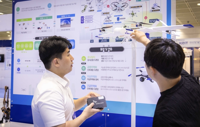 서울 코엑스에서 열리는 ‘무인이동체 산업엑스포 2024’에서 SKT와 원자력연구소 관계자가 불법 드론 대응 체계에 대해 대화하는 모습. (사진=SK텔레콤 제공)