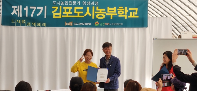 도시농업 전문가 양성교육을 받은 한 학생이 수료증을 받고 환하게 웃으며 기념사진을 찍고 있다. (사진=김포농업기술센터 제공)