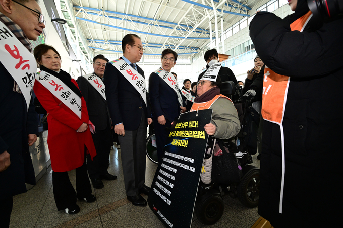 국민의힘 권영세 비상대책위원장과 권성동 원내대표가 24일 서울역에서 설 귀성인사를 하던 도중 전국장애인차별철폐연대 회원으로부터 항의를 받고 있다. (사진=연합뉴스)