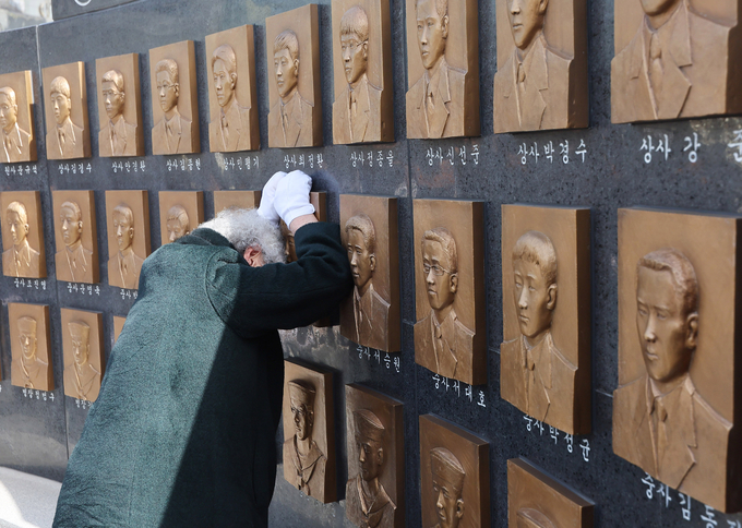 26일 오전 평택시 해군 제2함대 사령부에서 열린 '제15주기 천안함 46용사 추모식'에서 한 유가족이 추모비에 새겨진 얼굴에 기대어 슬픔에 빠져 있다.