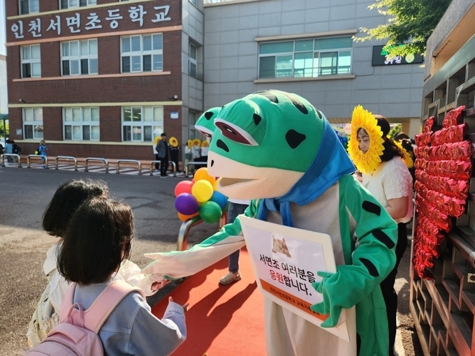 지난해 5월 인천 서면초등학교 교문 앞에서 개구리 인형탈을 쓴 김창용 교장이 학생들과 인사하고 있다. ( 사진 = 경기신문 DB )