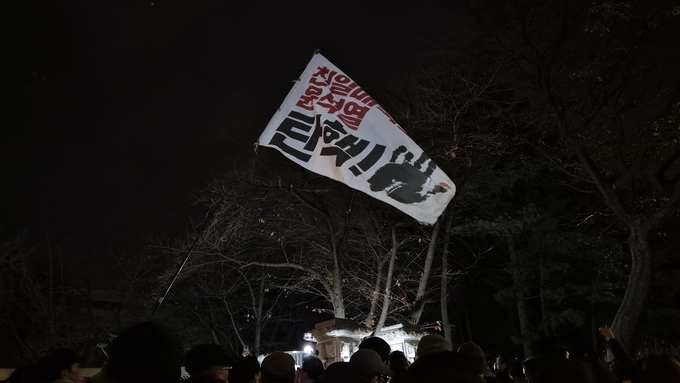 지난해 12월 4일 새벽 국회 앞에 모인 시민들이 깃발을 들고 윤석열 전 대통령 탄핵을 촉구하고 있다. (사진=김한별 기자)