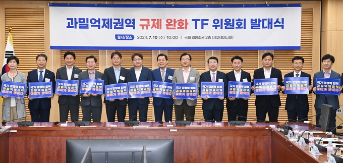 지난해 7월 국회에서 열린 ‘과밀억제권역 규제완화 TF 위원회 발대식’에서 참석자들이 과밀억제권역 완화를 위한 손팻말을 들고 있다. (사진=수원시 제공)