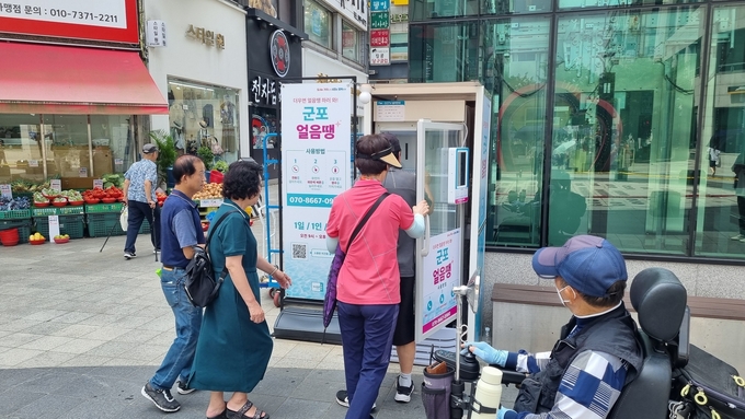 군포 시민들이 AI 무인 냉장고 ‘군포 얼음땡’에서 생수를 꺼내먹고 있다. (사진=군포시 제공)