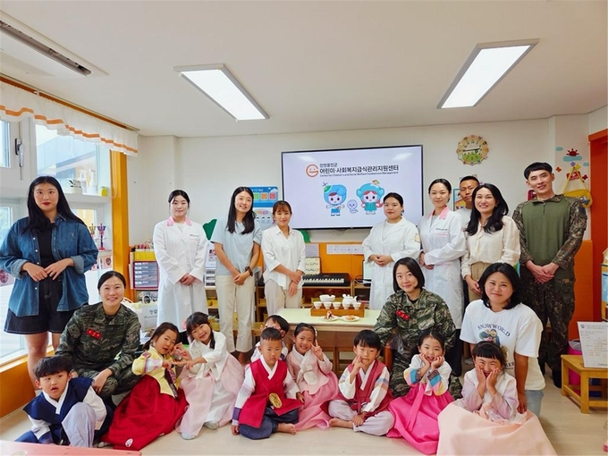 재능대학교 위탁 운영 인천옹진군 어린이·사회복지급식관리지원센터가 백령도 해병대흑룡어린이집에서 진행한 전통음식 체험 프로그램에 참여한 어린이들과 학부모, 군 장병, 센터 관계자들이 기념촬영을 하고 있다. ( 사진 = 재능대학교 제공 )