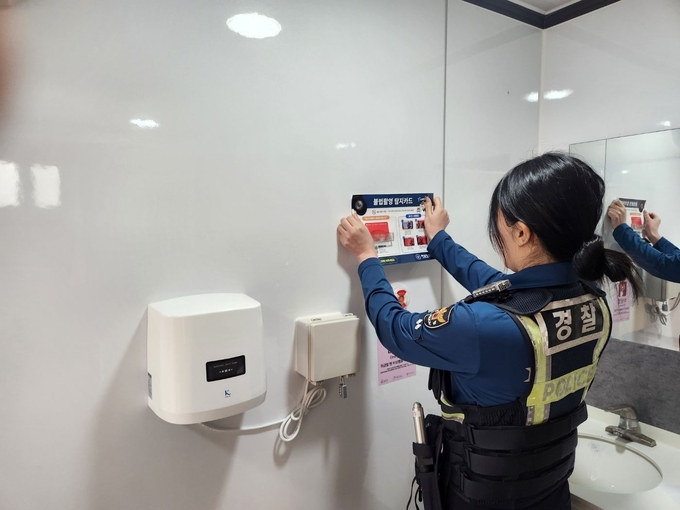 하남결찰서 한 경찰관이 감일문화공원 공중화장실 '불법카메라 탐지카드’를 알리는 안내문을 부착하고 있다. (사진=하남서 제공)